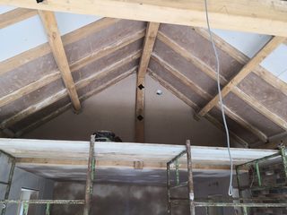 Fresh plaster to a gable and roof panels between exposed timber beams, with scaffolding below.
