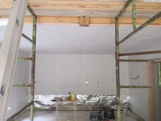 Boarded wall and ceiling below exposed timber beams, viewed through scaffolding.