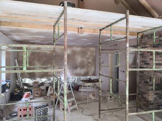 Fresh plaster to walls and ceiling below exposed timber beams, with scaffolding and equipment in the room.