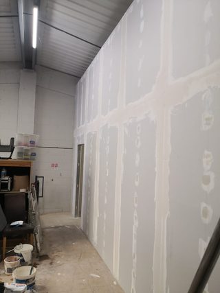 Boarded wall with jointing compound along the seams and over screw fixings, beside a doorway.