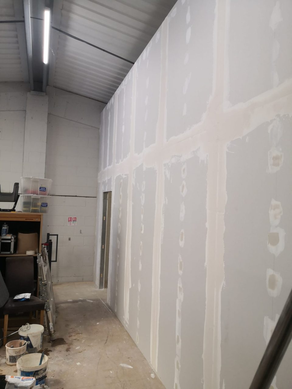 Boarded wall with jointing compound along the seams and over screw fixings, beside a doorway.