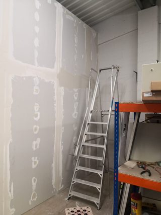 Plasterboard wall with filled joints and fixings beside storage racking and a stepladder.