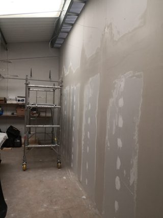Plasterboard wall with filled joints and fixings under a rooflight, beside a scaffold tower.