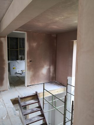Fresh plaster around a landing and stair opening with scaffolding and unfinished adjoining works.
