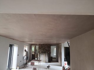 Freshly skimmed ceiling over a large room with a fireplace, boarded walls and plastering equipment.