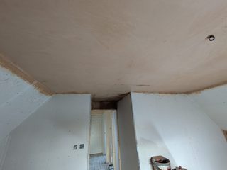 Fresh plaster on a ceiling above unfinished boarded walls and a doorway.