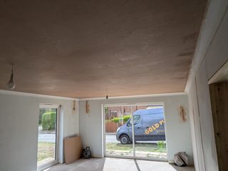 Freshly plastered ceiling above a room with a sliding patio door and unfinished wall repairs.