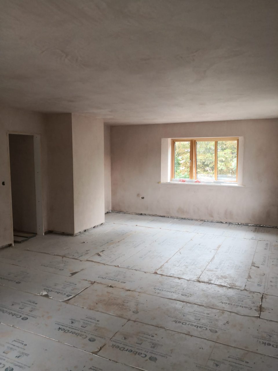Room with freshly plastered walls and ceiling, a timber-framed window and protected floor.