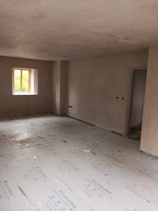 Freshly plastered walls and ceiling around a small timber-framed window, with floor protection in place.