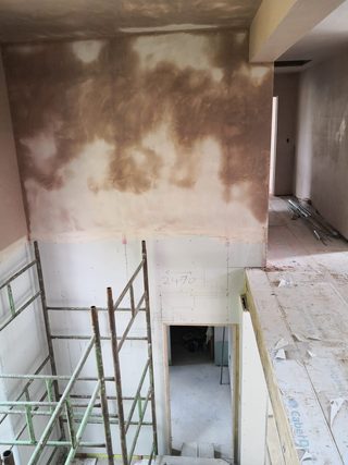 Stairwell with freshly plastered upper walls, unfinished lower plasterboard and scaffolding.