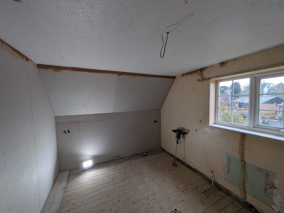 Textured ceiling above boarded sloping walls in a room being prepared for plastering.