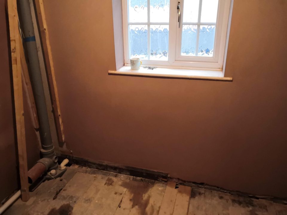 Freshly plastered wall around a frosted window, with exposed pipework at the left.