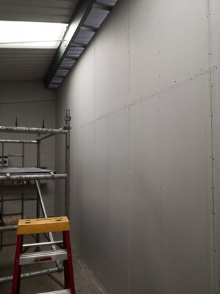 Boarded wall beneath a rooflight with visible board seams and screw fixings, beside scaffolding.